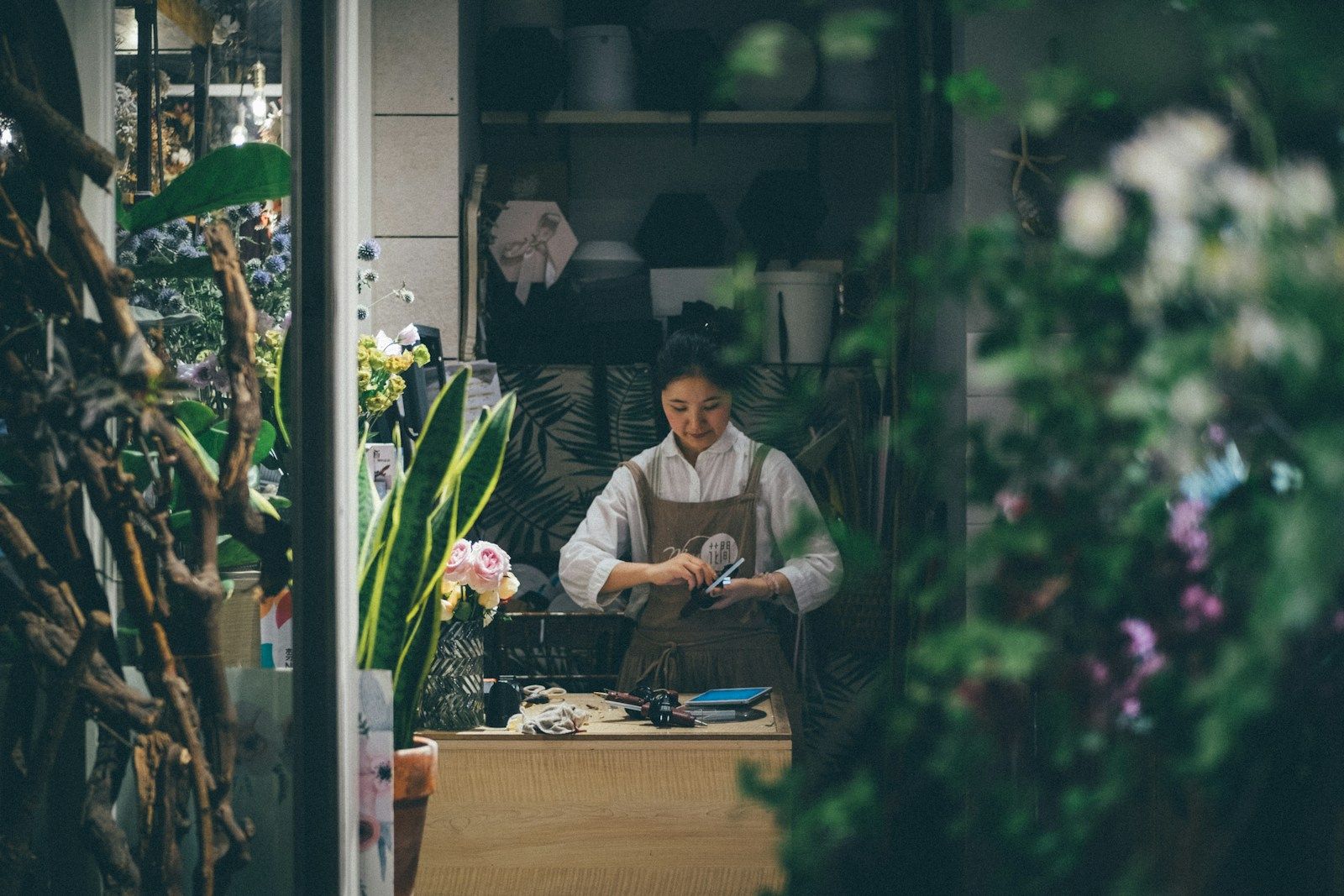 A small-business owner working at the counter of her own shop, seen from the street